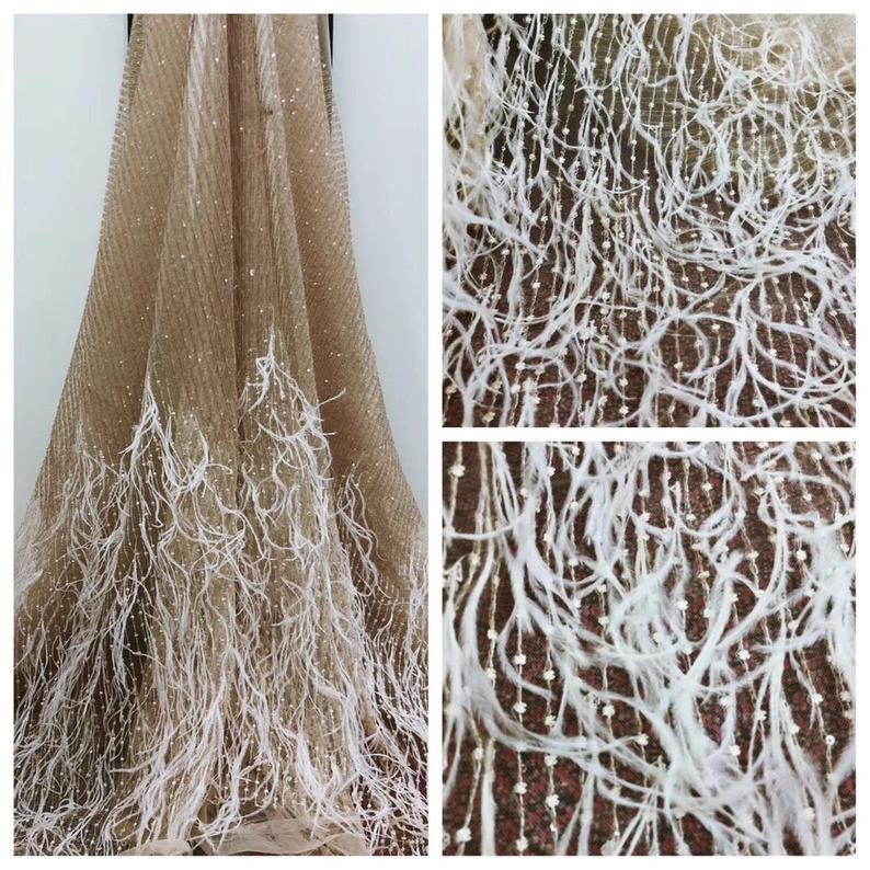 May include: Beige mesh fabric with white feather trim and small sequins. The fabric is sheer and has a delicate texture.
