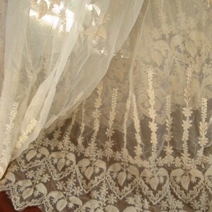 May include: White sheer fabric with delicate embroidered floral patterns. The fabric has a scalloped edge and is perfect for crafting or decorating.