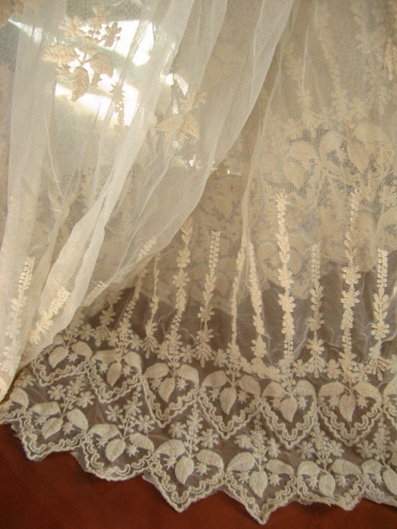 May include: White sheer fabric with delicate embroidered floral patterns. The fabric has a scalloped edge and is perfect for crafting or decorating.