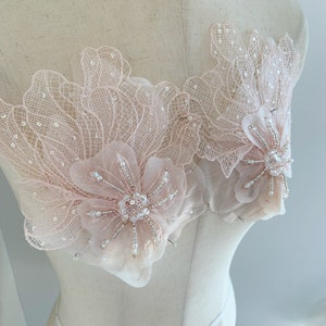 May include: Two delicate pink floral appliques with pearl and silver bead embellishments. The appliques are on a white dress form.