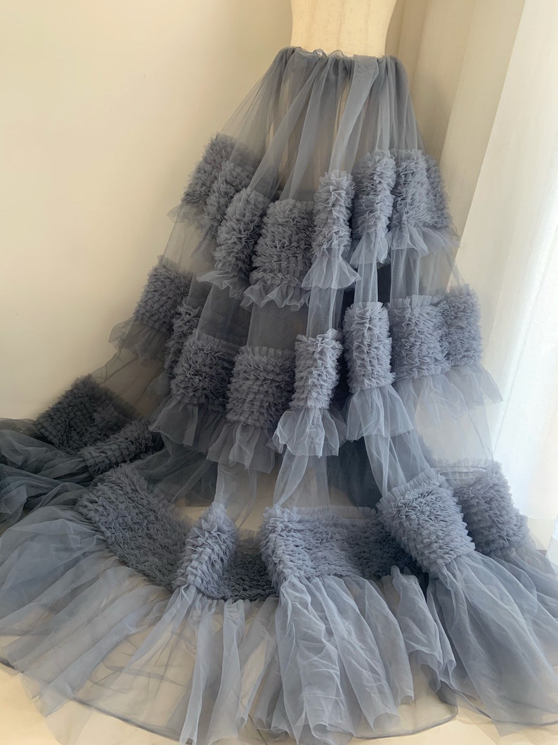 May include: A gray tulle skirt with multiple layers of ruffles. The ruffles are made of a soft, textured fabric and create a voluminous look.