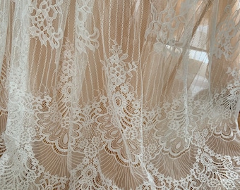 May include: White lace fabric with a delicate floral pattern. The lace has a scalloped edge and is sheer and lightweight.