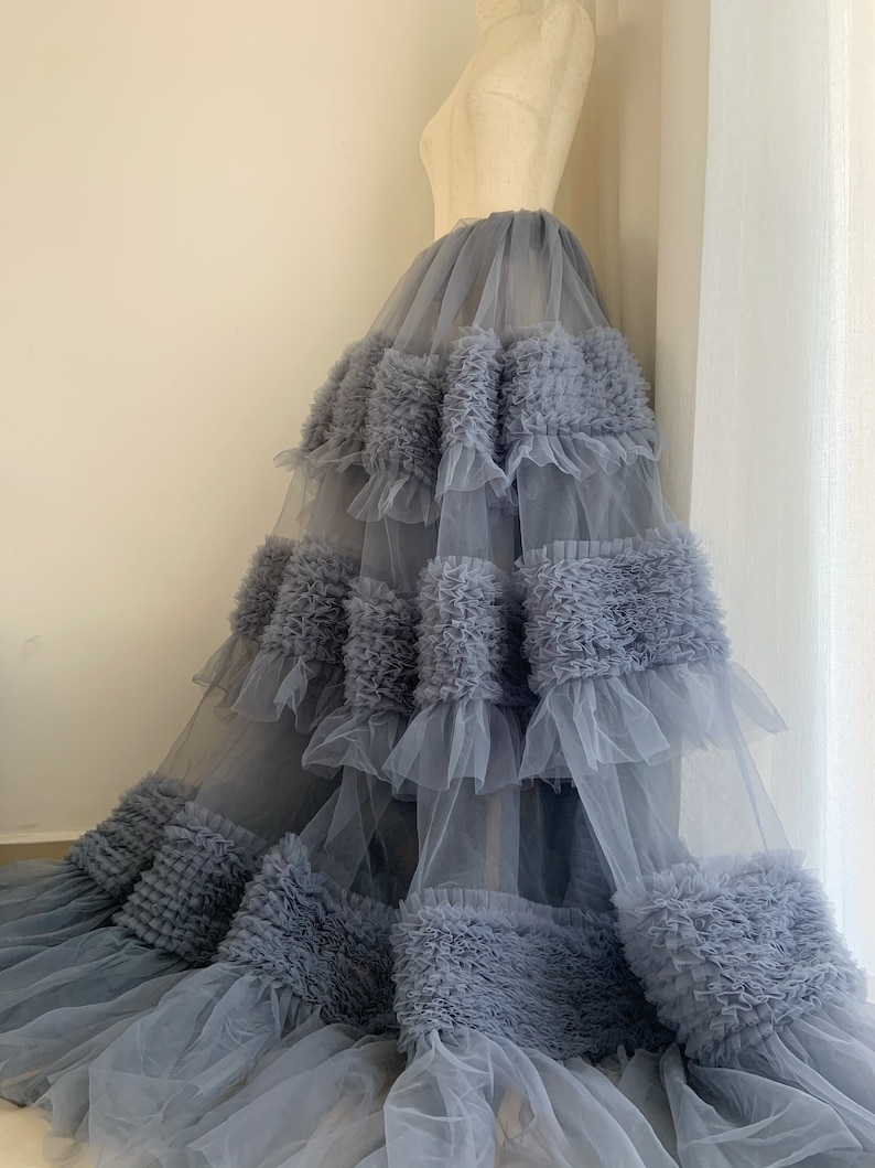 May include: A gray tulle skirt with multiple layers of ruffles. The skirt is full and flowing, with a soft, romantic look.
