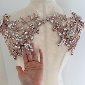 Puede incluir: Aplicación decorativa para el hombro con diseño floral. La aplicación está hecha de cuentas de color oro rosa y cristales transparentes, dispuestas sobre un respaldo de malla transparente. El diseño simétrico está destinado al embellecimiento.