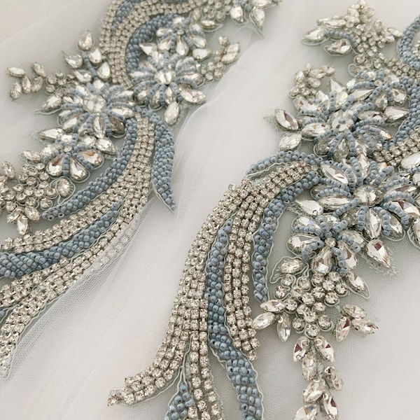 May include: Two delicate, light blue and silver beaded appliques with a floral design. The appliques are made with small, sparkling rhinestones and beads.