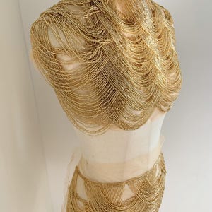 Könnte beinhalten: Ein goldfarbenes Perlen-Oberteil und Rock-Set. Das Oberteil ist im Halterneck-Stil mit hohem Ausschnitt und der Rock ist ein Minirock mit hoher Taille.