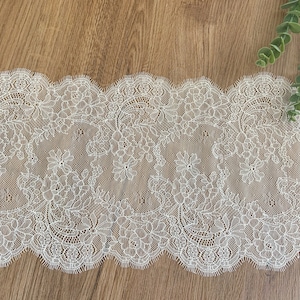 May include: White lace trim featuring a delicate floral design. The lace has a scalloped edge and is ideal for adding a touch of elegance to any project.