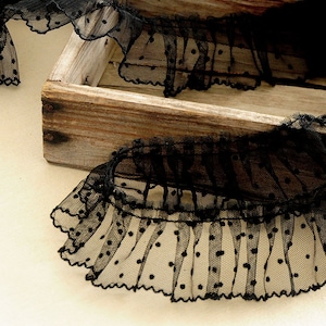 May include: Black lace trim with polka dots, shown in a wooden box. The lace is ruffled and has a delicate, vintage look.