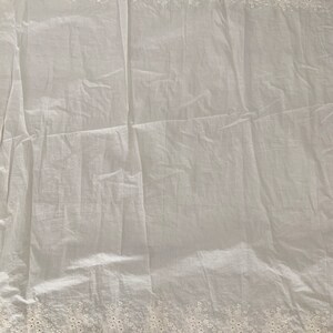 May include: White cotton fabric with a delicate white lace trim. The fabric is slightly wrinkled and has a soft, airy feel.