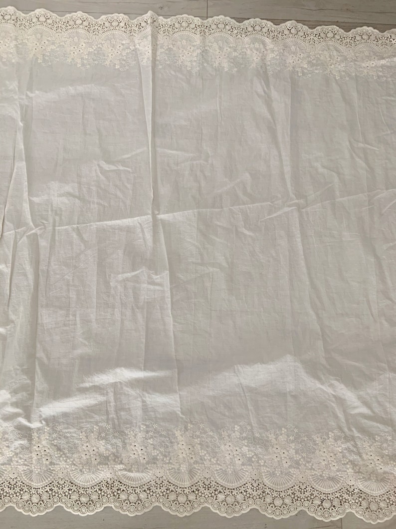 May include: White cotton fabric with a delicate white lace trim. The fabric is slightly wrinkled and has a soft, airy feel.