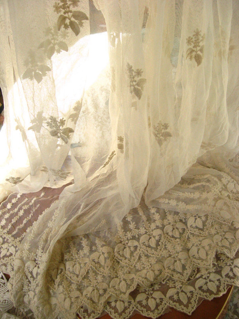 May include: White sheer curtains with delicate floral embroidery. The curtains are gathered at the bottom, creating a soft, flowing look.