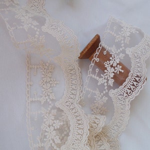 May include: A spool of ivory-coloured lace trim with a delicate floral pattern. The lace is soft and sheer, with a scalloped edge.