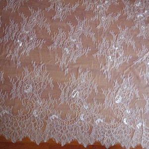 May include: White lace fabric with a delicate floral pattern. The lace has a scalloped edge.