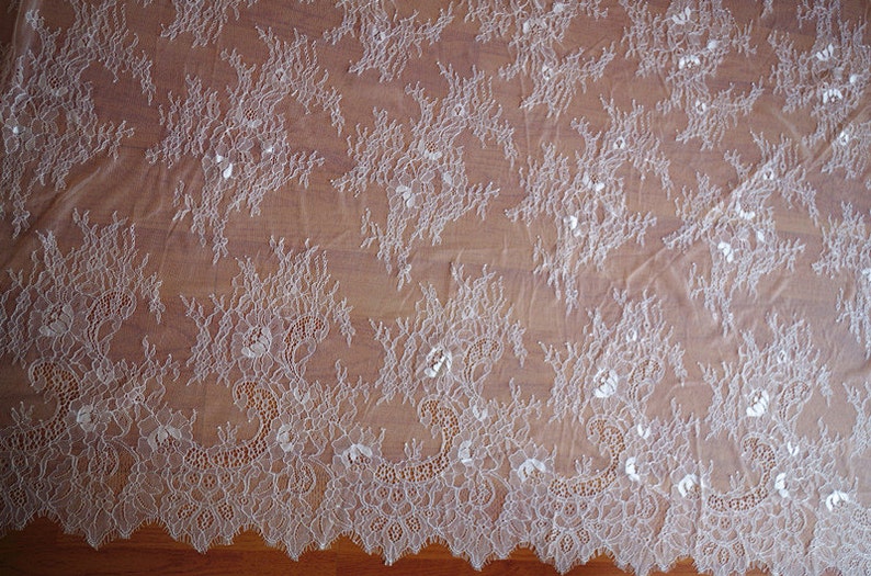 May include: White lace fabric with a delicate floral pattern. The lace has a scalloped edge.