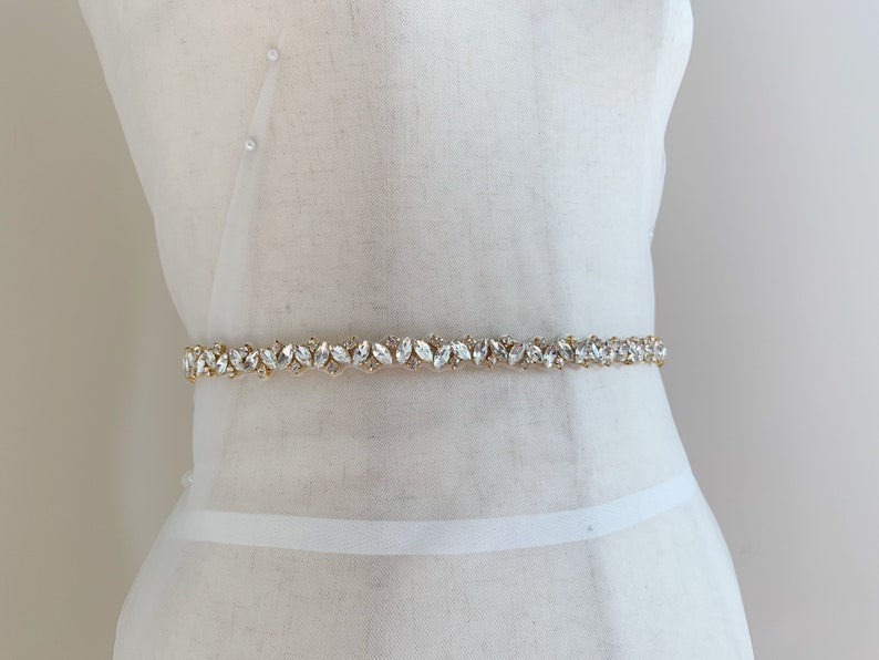 Puede incluir: Un cintur&oacute;n de novia dorado con adornos de cristal transparente en forma de hoja.