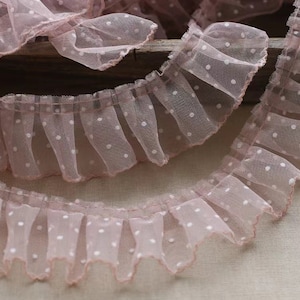 Puede incluir: Borde de encaje de tul rosa con lunares y borde rizado. El encaje es delicado y tiene un aspecto suave y femenino.