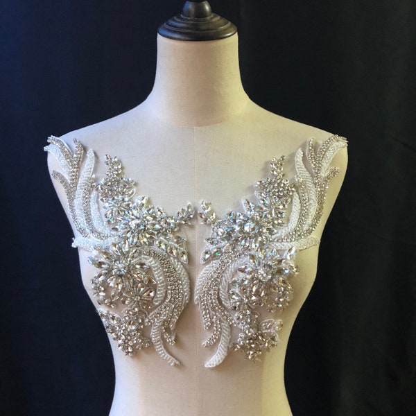 May include: A pair of silver rhinestone embellishments with a floral design. The embellishments are on a white background.