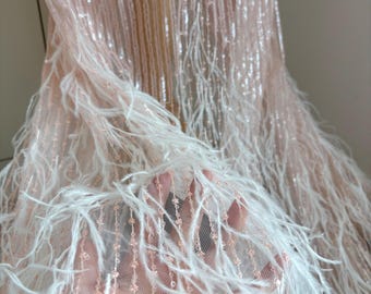 Puede incluir: Primer plano de una tela rosa pálido con filas verticales de lentejuelas. Plumas blancas se superponen en la parte inferior, creando un efecto suave y texturizado. La tela parece ser parte de un vestido o prenda.