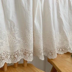 May include: White cotton curtains with a delicate white lace trim. The curtains are gathered at the top and have a ruffled edge.