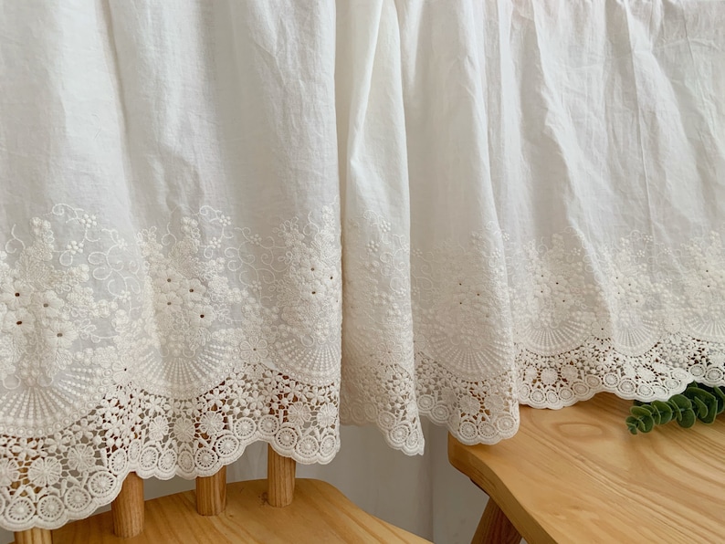 May include: White cotton curtains with a delicate white lace trim. The curtains are gathered at the top and have a ruffled edge.