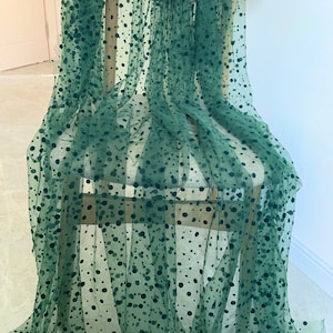 Może przedstawiać: Zielony, przezroczysty materiał w czarne kropki. Materiał jest udrapowany na drewnianym krześle.