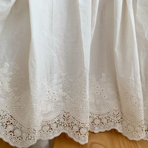 May include: White cotton bed skirt with a delicate white lace trim and embroidered floral details.