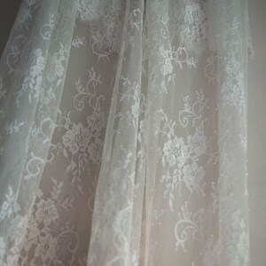 May include: White lace fabric with a floral pattern. The fabric is sheer and delicate, with a soft, flowing texture.