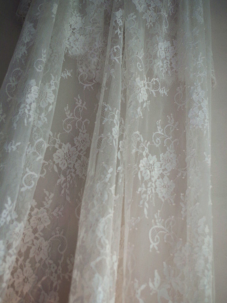 May include: White lace fabric with a floral pattern. The fabric is sheer and delicate, with a soft, flowing texture.