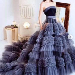 May include: A strapless, layered tulle gown with a black bodice and a ruffled skirt. The skirt is made of multiple layers of tulle, creating a voluminous and dramatic look.