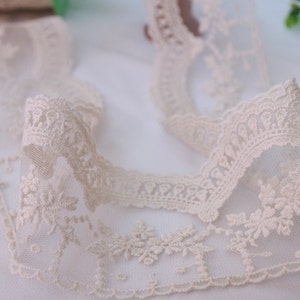 May include: A close-up of a delicate, off-white lace trim with a floral pattern. The lace is soft and sheer, with a delicate texture. It is perfect for adding a touch of elegance to any project.