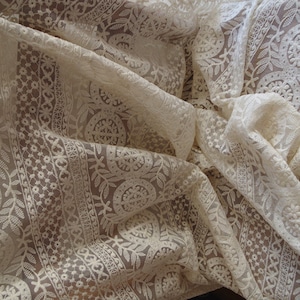 Peut inclure: Tissu de dentelle blanc avec un motif floral d&eacute;licat. Le tissu est transparent et a une texture douce et fluide.