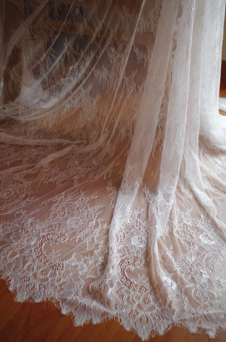 May include: White lace fabric with a delicate floral pattern. The lace is sheer and has a soft, flowing texture.