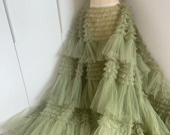 May include: A sage green tulle skirt with multiple layers of ruffles. The skirt is made of a soft, sheer fabric and has a flowing, romantic silhouette.