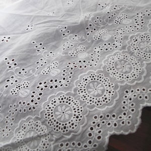 May include: White cotton fabric with a delicate embroidered design featuring floral motifs and scalloped edges.