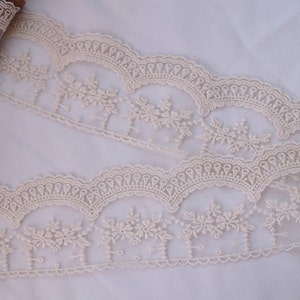 May include: Ivory lace trim with a scalloped edge and floral embroidery. The lace is delicate and intricate, with a soft, feminine feel.