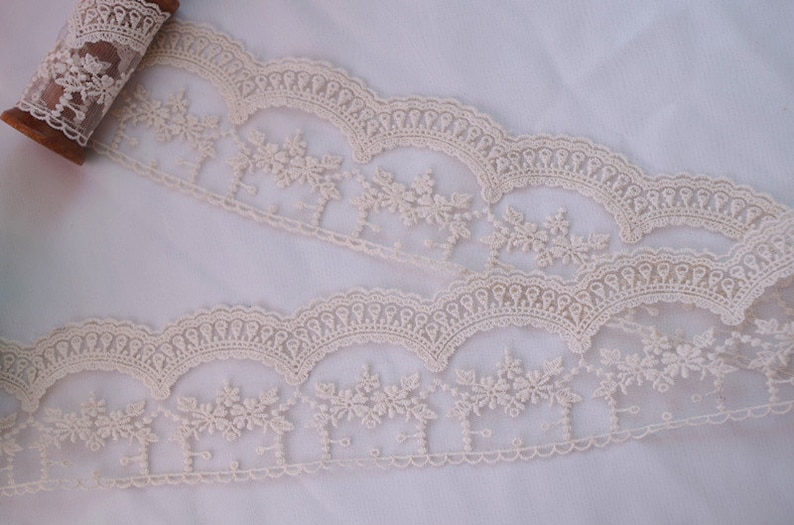 May include: Ivory lace trim with a scalloped edge and floral embroidery. The lace is delicate and intricate, with a soft, feminine feel.