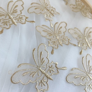 May include: Gold butterfly embroidery on a white tulle fabric. The butterflies are delicate and intricate, with detailed wings and bodies.