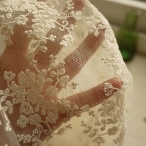 Puede incluir: Tela de encaje blanca con un delicado patr&oacute;n floral. El encaje es transparente y tiene un tacto suave y rom&aacute;ntico.