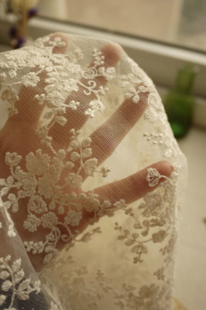 Puede incluir: Tela de encaje blanca con un delicado patr&oacute;n floral. El encaje es transparente y tiene un tacto suave y rom&aacute;ntico.