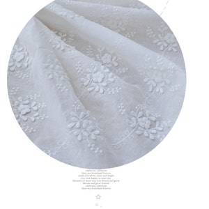 May include: White cotton fabric featuring a delicate floral embroidery pattern. The fabric is sheer and lightweight, with a soft, flowing texture.