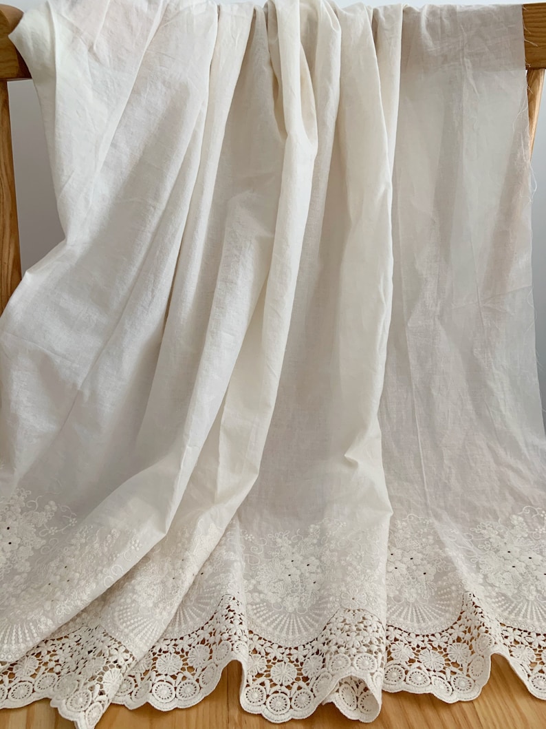 May include: White cotton fabric with a delicate lace trim. The lace features a floral design with small circles and scalloped edges.