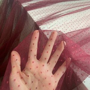 May include: Burgundy red tulle fabric with small white polka dots. The fabric is sheer and delicate.
