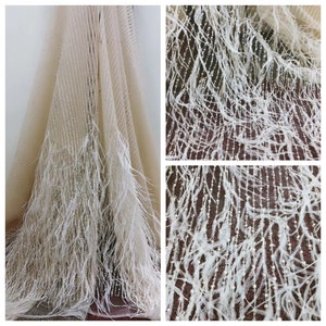 May include: Beige tulle fabric with white feather trim and a beaded design. The fabric is sheer and has a delicate texture.