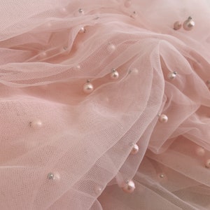 Puede incluir: Tela de tul rosa con adornos de perlas. La tela es suave y delicada, y las perlas añaden un toque de elegancia.