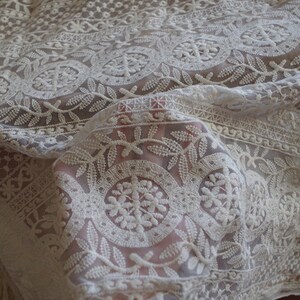 Peut inclure: Tissu de dentelle blanche avec un motif floral d&eacute;licat. Le tissu est transparent et a une texture douce et fluide.