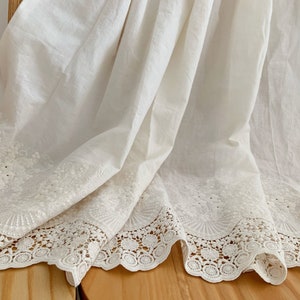 May include: White cotton fabric with a delicate lace trim. The fabric has a subtle embroidered pattern.