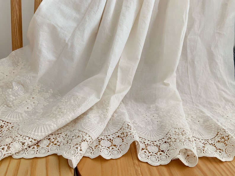 May include: White cotton fabric with a delicate lace trim. The fabric has a subtle embroidered pattern.