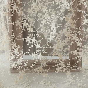 May include: Ivory floral lace fabric with a delicate pattern of small flowers and branches. The lace is sheer and has a soft, romantic feel.