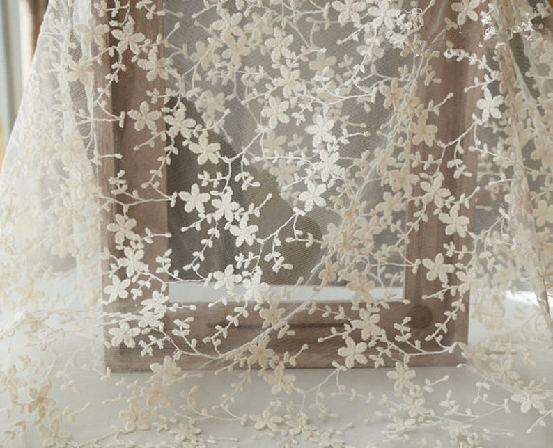 May include: Ivory floral lace fabric with a delicate pattern of small flowers and branches. The lace is sheer and has a soft, romantic feel.