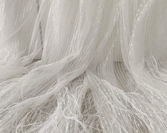 Puede incluir: Tela de tul blanco con una textura delicada de plumas y un brillo sutil. La tela es transparente y ligera, lo que la hace ideal para crear una variedad de prendas y accesorios.